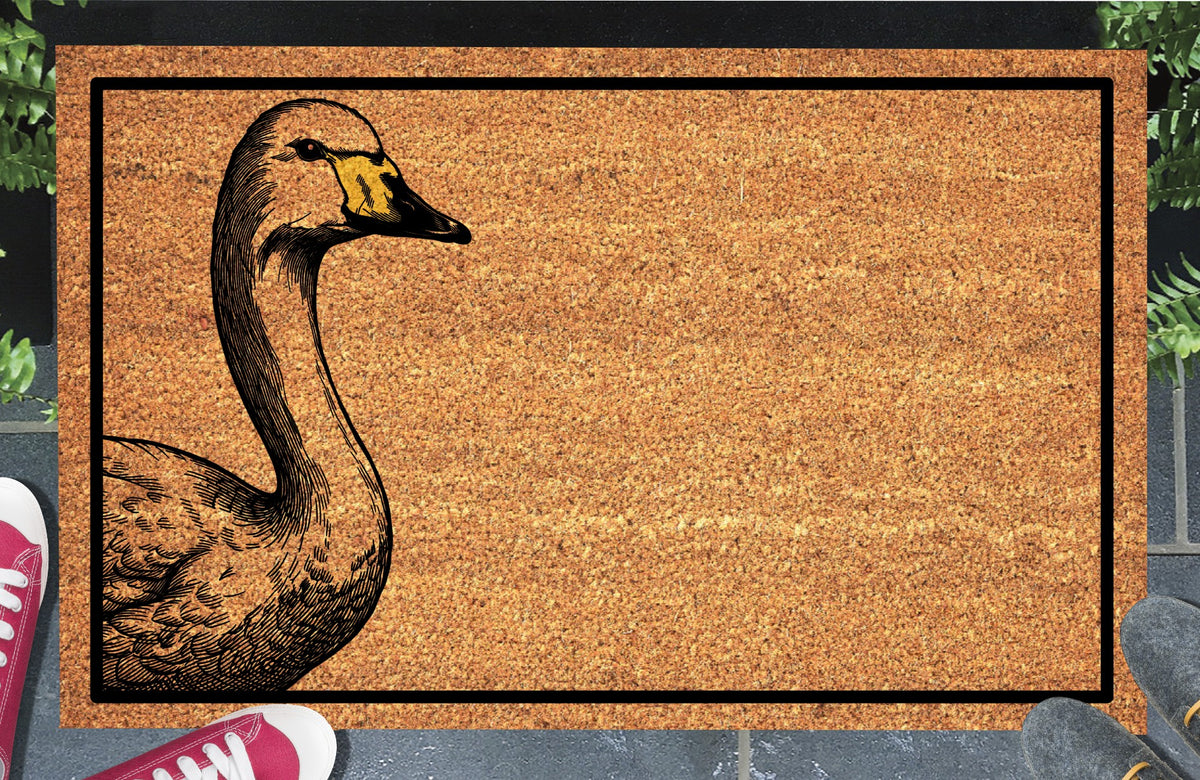 Whooper Swan peeking from the left edge of a natural coir doormat, showing a long curved neck, feathered body and yellow-and-black bill within a black border, at a doorstep.